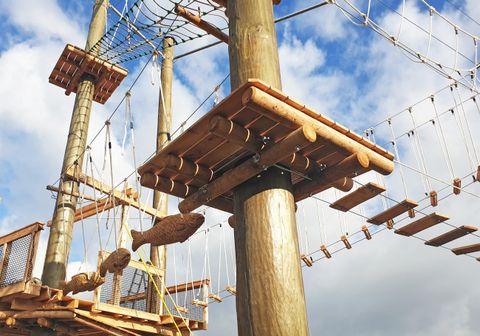 Ein Klettergerüst aus Holz mit Plattformen und Seilbrücken. Der Himmel ist wolkig und es gibt viele Kletterelemente.