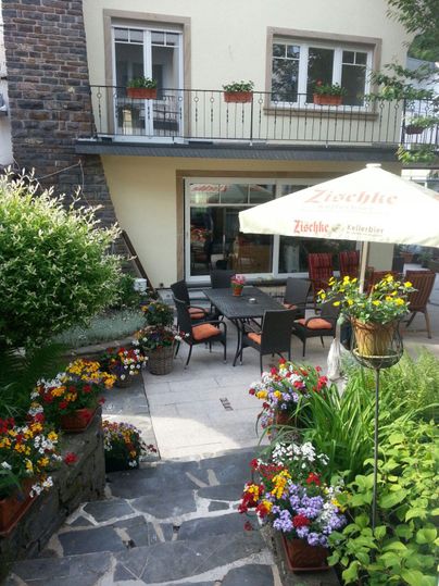 Ein einladender Garten mit bunten Blumen und einer gemütlichen Terrasse. Im Hintergrund befindet sich ein Haus mit einem Balkon.