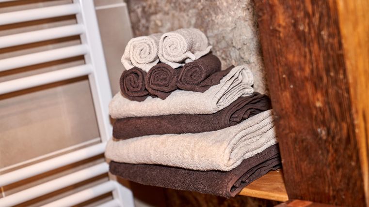 A stack of towels in various colors, neatly arranged on a shelf. In the background, a radiator is visible.