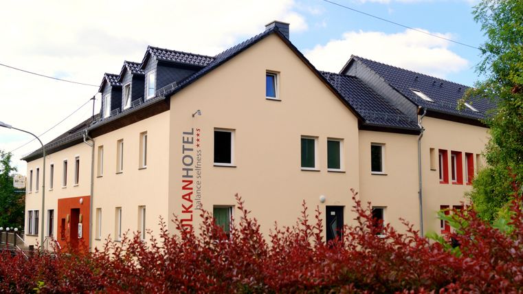 A modern hotel building with a clear, friendly design. In the foreground, there are multicolored bushes that create an inviting atmosphere.