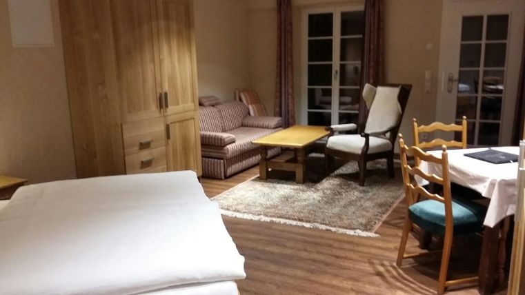 A cozy room with wooden furniture and a large window. There is a bed, a seating area, and a dining table.