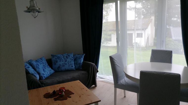 Een gezellige woonruimte met een bank en tafel. Grote ramen bieden uitzicht op de tuin.