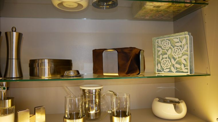 A shelving system with various kitchen utensils and decorative items.Among them are glasses, a teapot, and an elegant decoration book.