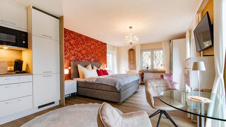 Ein modernes Zimmer mit einem großen Bett und eleganter Einrichtung. Eine gemütliche Sitzecke und große Fenster sorgen für viel Licht.