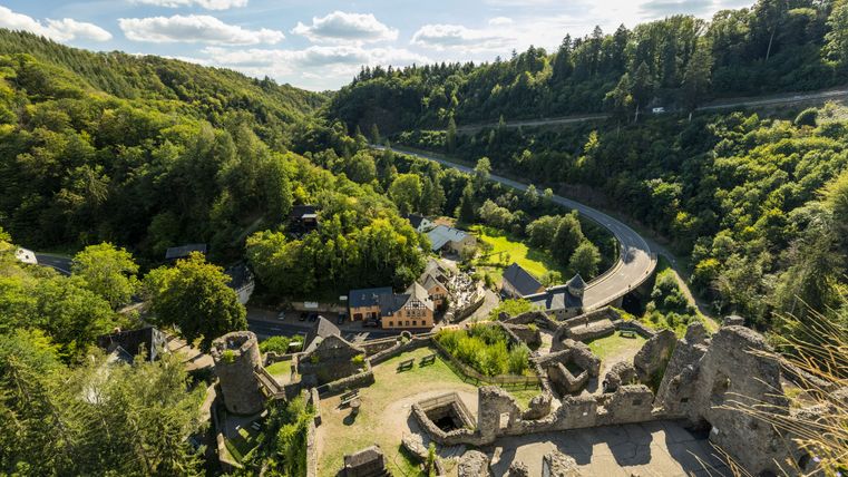 Blick von der Niederburg Manderscheid auf eine grüne Landschaft mit Ruinen und einer Straße.
