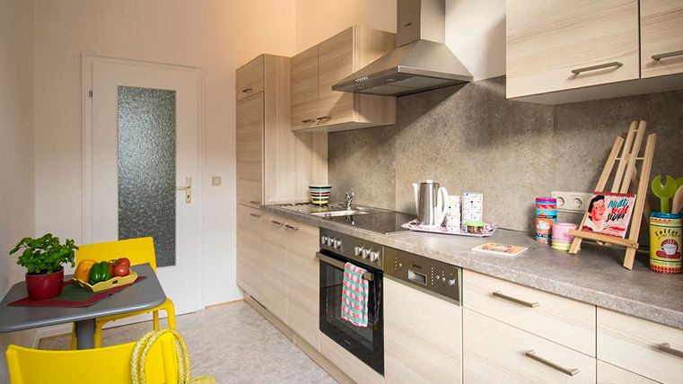 Eine moderne Küche mit hellen Holzmöbeln und einem praktischen Layout. Auf dem Tisch stehen frisches Gemüse und eine gelbe Tasche.