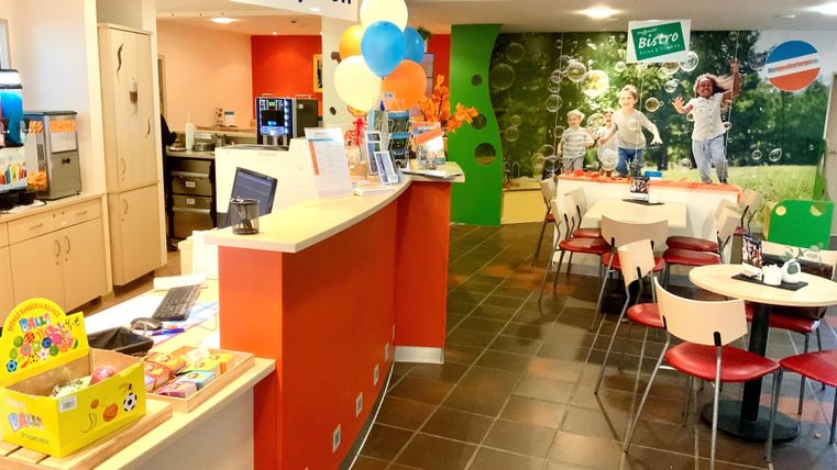 Blick auf das Bistro drinnen. Aufstellt sind kleine Tische und Stühle. nebenan findet man de Rezeption