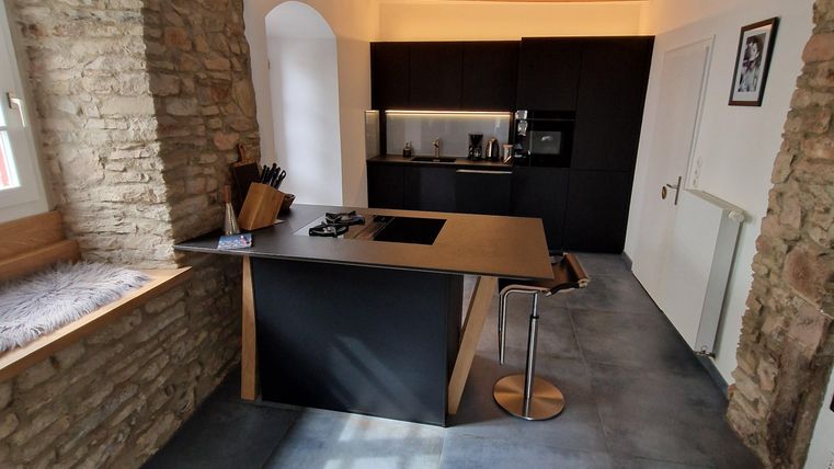 A modern kitchen with a wooden ceiling and stone wall. It features a central cooking island and modern appliances.