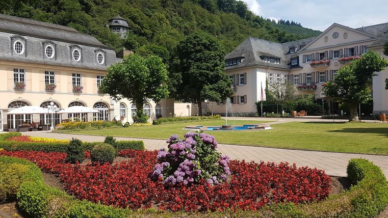 Een mooie tuin met kleurrijke bloembedden en verzorgde gazons. Op de achtergrond zijn elegante gebouwen en groene bomen te zien.