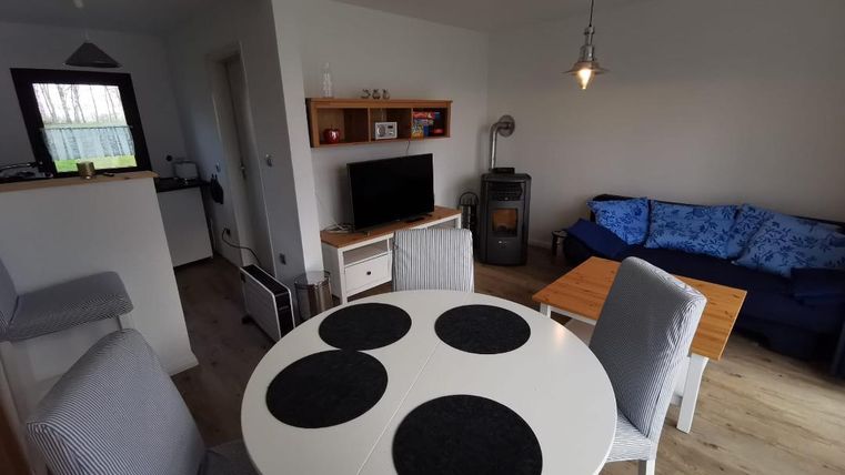 Een gezellige woonkamer met een ronde eettafel, stoelen en een blauwe bank. De kamer heeft lichte muren en een houten vloer, waardoor het vriendelijk aanvoelt.