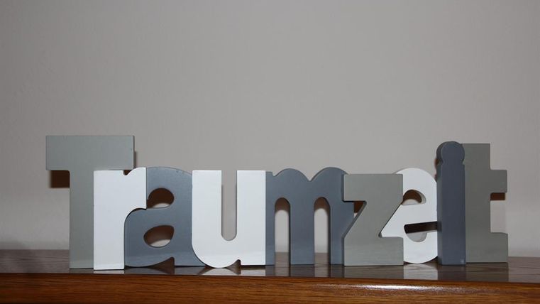 A decorative lettering made of colorful letters that form the word "Traumzeit". The background is simple and neutral.
