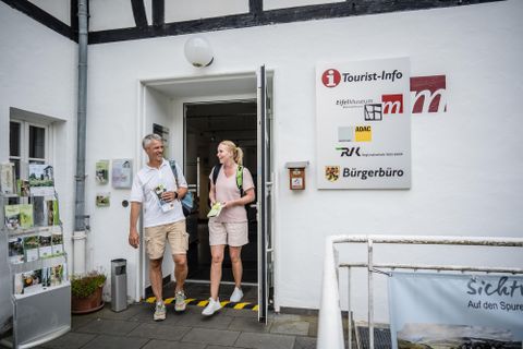 Een paar verlaat het toeristeninformatiecentrum. Op de achtergrond zijn informatiestands en borden zichtbaar.
