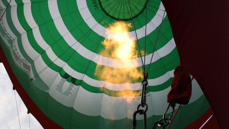 A look inside a hot air balloon with green and white stripes. Flames unfold beneath the balloon and generate heat.
