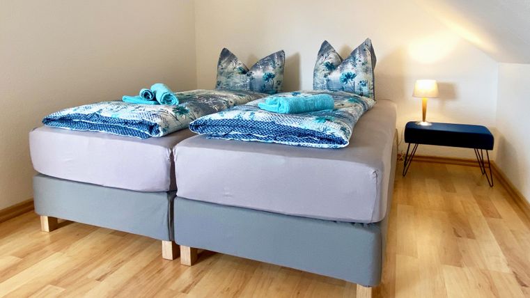 Ein gemütliches Schlafzimmer mit zwei getrennten Betten und dekorativen Kissen. Neben den Betten steht ein Tisch mit einer Lampe und Holzfußboden.