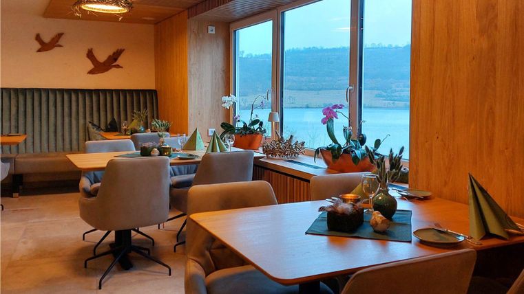 Ein modernes Café mit Holzwänden und großen Fenstern. Es gibt gemütliche Sitzplätze und dekorative Pflanzen.