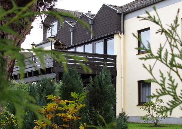 Ein gemütliches Haus mit einem Balkon und großen Fenstern. Umgeben von grünen Pflanzen und Sträuchern.