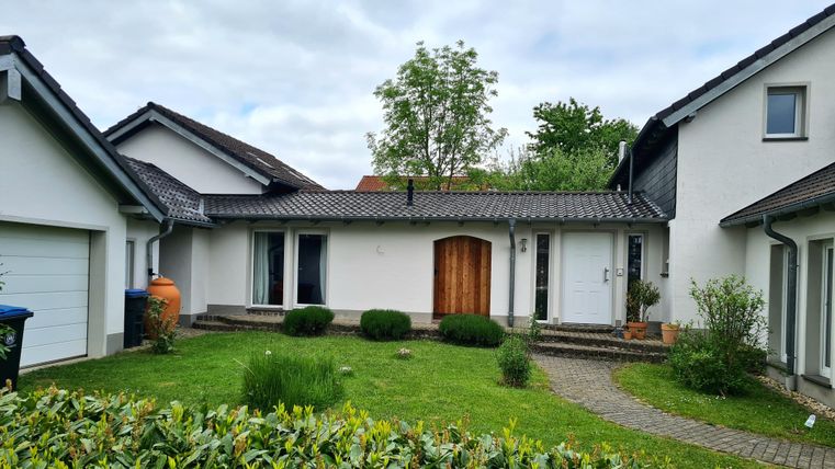 Ein einladendes Haus mit einer schönen Eingangstür und gepflegtem Garten. Umgeben von Bäumen und modernen Gebäuden.