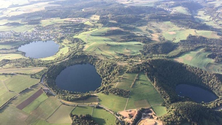 Een indrukwekkend landschap met twee grote meren en omringende weiden en velden. Op de achtergrond zijn zachte heuvels en een heldere lucht te zien.