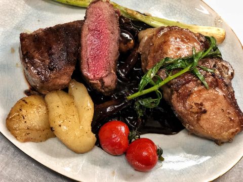 Een heerlijk bord met zacht vlees, dat rosé gebraden is. Daarbij zijn er aardappelen, cherrytomaten en een groene garnering.
