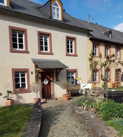 Ein charmantes Haus mit einem begrünte Vorgarten. Die Fassade ist hell und mit braunen Fensterrahmen gestaltet.