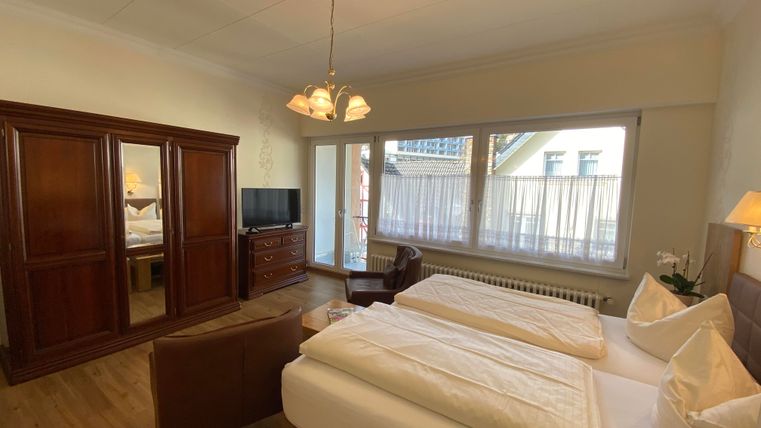 Ein helles Hotelzimmer mit zwei Betten und Holzmöbeln. Große Fenster bieten viel Tageslicht und eine gemütliche Atmosphäre.