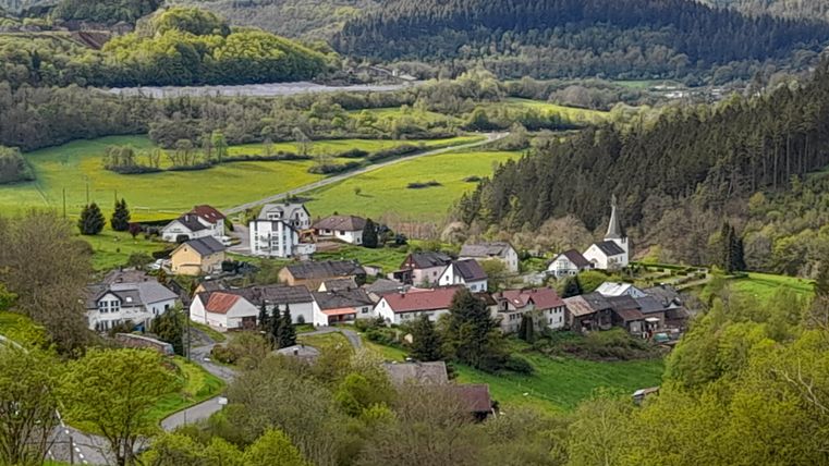 A picturesque village surrounded by green meadows and forests. The landscape is idyllic and hilly.