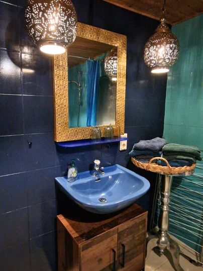 A stylish bathroom with a blue washbasin and a beautiful mirror. Ceiling lights and a green wall give the room a cozy atmosphere.