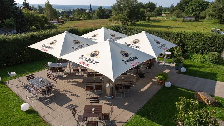 A cozy terrace with sun umbrellas and wooden chairs. In the background, a green landscape can be seen.