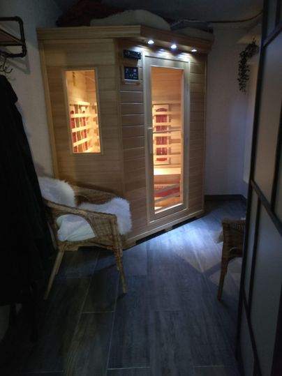 A cozy sauna in a modern room, equipped with a wooden bench and indirect lighting. Next to it are two chairs for relaxation.