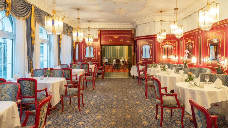 Een elegant restaurant met rode muren en stijlvolle meubels. De tafels zijn liefdevol gedekt en de verlichting is warm en uitnodigend.