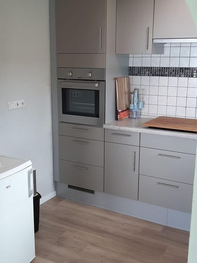 Eine moderne Küche mit grauen Schränken und hellen Wänden. Auf der Arbeitsfläche stehen Küchenutensilien und eine Spüle.