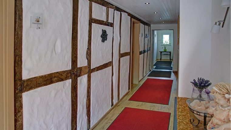 Ein langer Flur mit Holzrahmen und weißen Wänden. Rote Teppiche verleihen dem Raum eine einladende Atmosphäre.