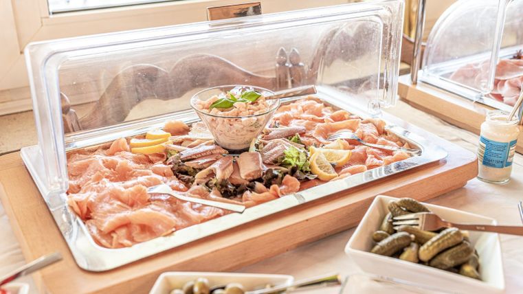 A buffet with various types of fish and shrimp, garnished with herbs and lemons. Next to the fish are bowls of olives and pickles.