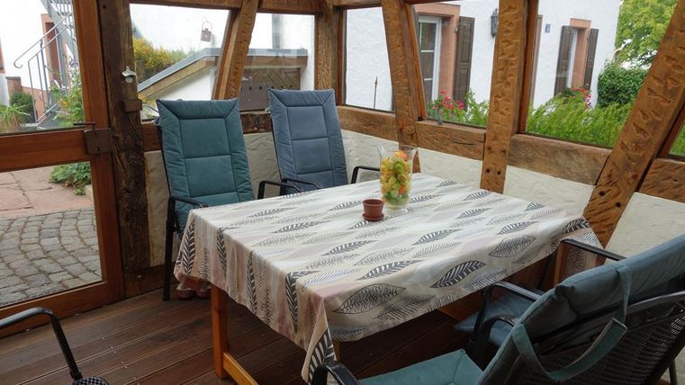 Een gezellige ruimte met glazen wanden, een houten tafel en twee stoelen. Op de tafel staat een plant en een kleine decoratie.