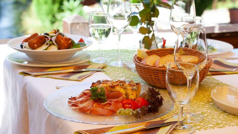 Ein schön gedeckter Tisch mit köstlichem Essen und Wein. Im Hintergrund sind frische Blumen und ein Korb mit Brot zu sehen.