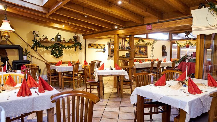 Ein gemütliches Restaurant mit Holzbalkendecke und hellen Tischen. Die Tische sind mit roten Servietten dekoriert und die Wände sind festlich geschmückt.