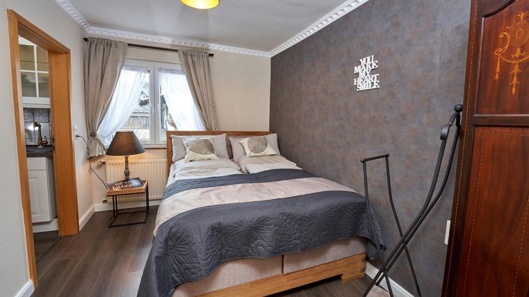 A cozy bedroom with a double bed and decorative pillows. The walls are painted in soft colors, and there is a small table as well as a wardrobe.