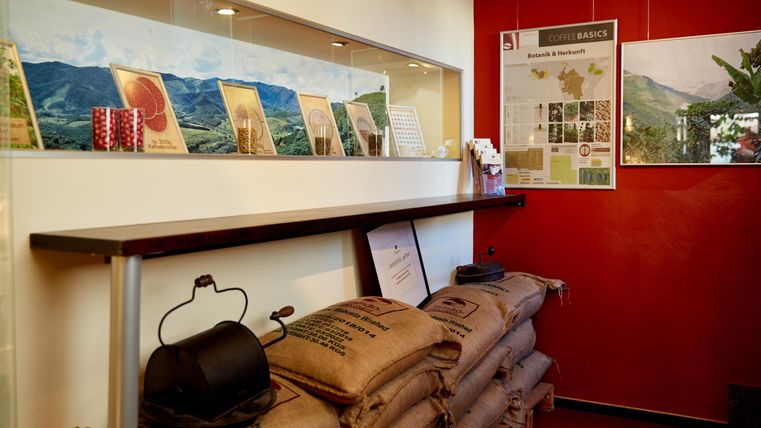 Ein gemütlicher Verkaufsraum mit gerösteten Kaffeebohnen und einer Auslage von Informationsmaterialien. Die Wände sind rot gestrichen und mit Bildern dekoriert.