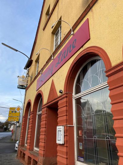 Een gebouw met een oranje gevel en grote, gewelfde ramen. Boven de ingang hangt een bord met de naam van het restaurant.