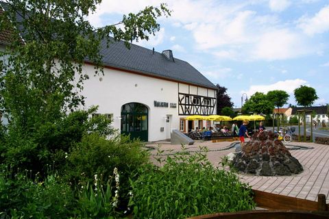 Ein charmantes Gebäude mit traditionellen Elementen und einer einladenden Terrasse. Der Außenbereich ist grün und lädt zum Verweilen ein.