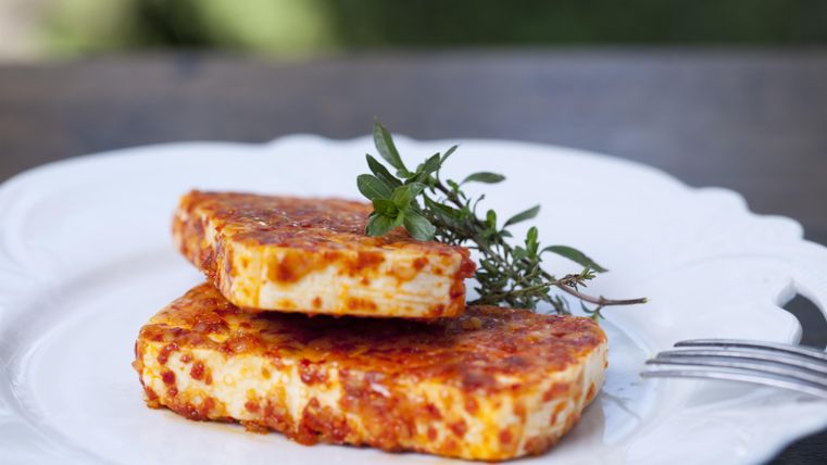 Ein Teller mit zwei Stück gebratenem Käse, garniert mit frischen Kräutern. Der Käse hat eine goldene, knusprige Oberfläche.