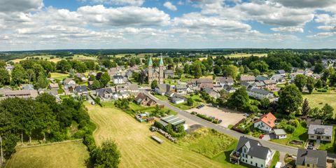 Eine ruhige Landschaft mit einem kleinen Dorf und einer Kirche im Zentrum. Rund um das Dorf befinden sich grüne Felder und Bäume.