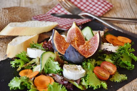 Salad plate topped with green lettuce, tomatoes, cucumber slices, fig, carrot slices, and round cheese slices. At the edge of the square black plate are two slices of baguette.
Symbol image