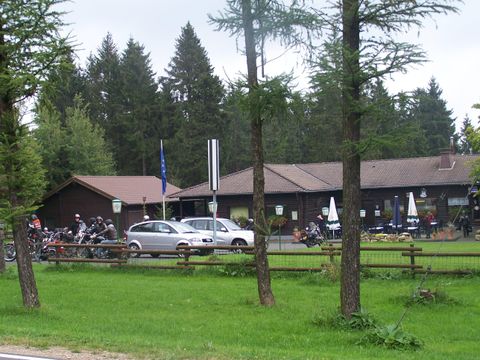 Ein gemütliches Gasthaus umgeben von Bäumen. Es stehen viele Fahrräder und Autos vor dem Gebäude.