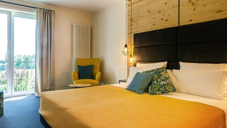 Een comfortabele kamer met een groot bed en een gezellige zithoek. De ramen laten veel licht binnen en bieden uitzicht naar buiten.