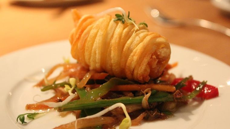 Een kunstzinnig opgemaakt gerecht met gefrituurde groenten en een knapperige rol. Daarbij verse kruiden en kleurrijke groentesticks.