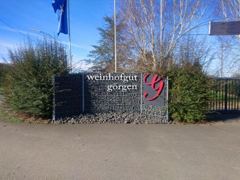 Een ingangsbord naar de wijngoed Gorgen, omringd door groene struiken. De lucht is blauw en helder.