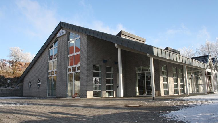 A modern building with large windows and a slanted roof. The sky is clear and there is snow on the ground.