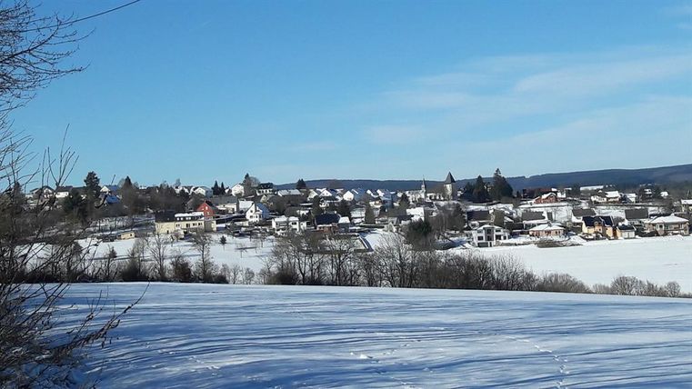 Eine verschneite Landschaft mit einem kleinen Dorf im Hintergrund. Der Himmel ist klar und blau.