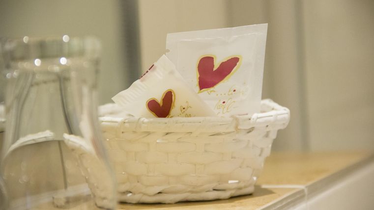 Een witte mand met papieren handdoeken, waarop rode harten zijn geschilderd. De mand staat op een houten plank.
